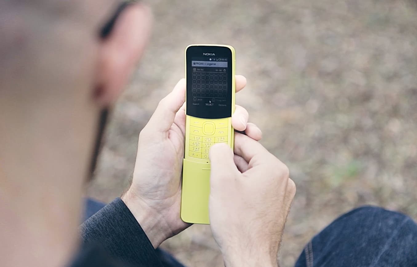Um homem jogando PROXX em um feature phone amarelo