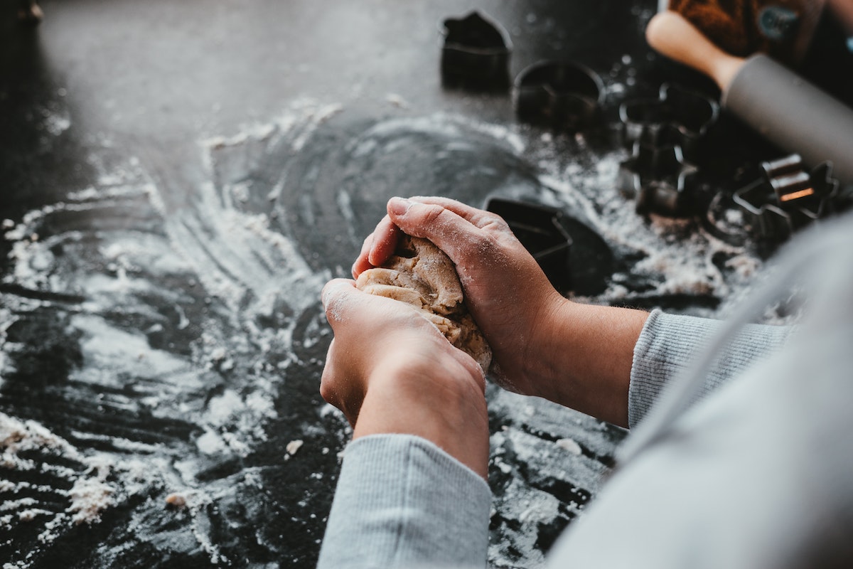 A person kneading dough on a kitchen table covered in flour